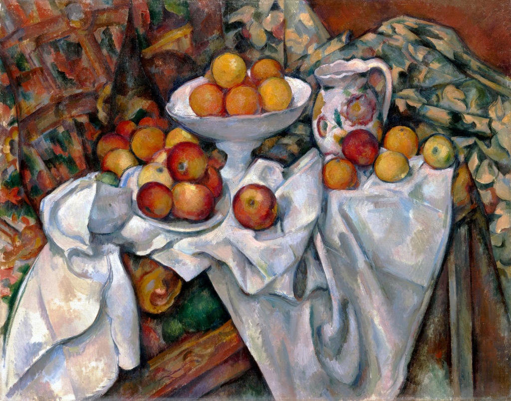 Cezanne's painting of oranges in dishes sitting on white fabric on a patterned chair. 